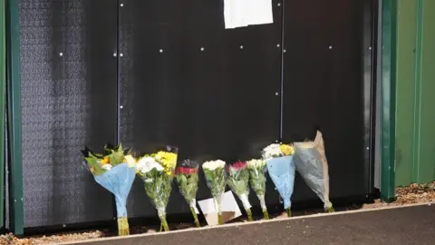 Bảy bó hoa đặt trước bức tường đen tưởng nhớ Billy Vigar