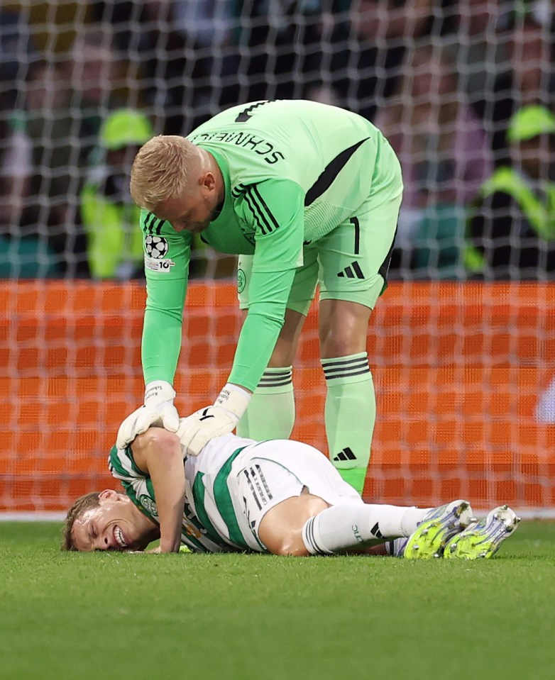 Alistair Johnston of Celtic lies injured on the ground with a teammate bending over him during a football match.