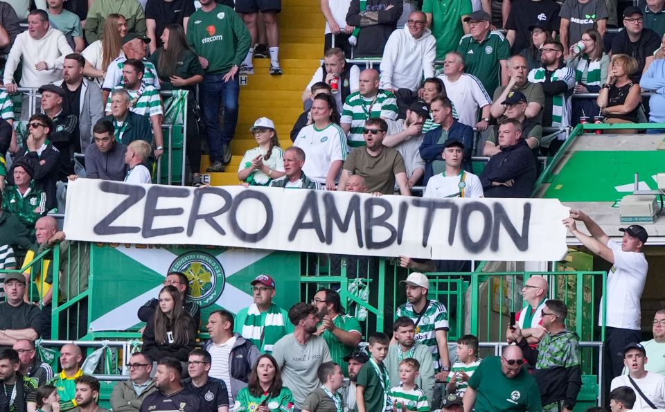 Celtic fans holding a banner that reads 'ZERO AMBITION' at a football match.